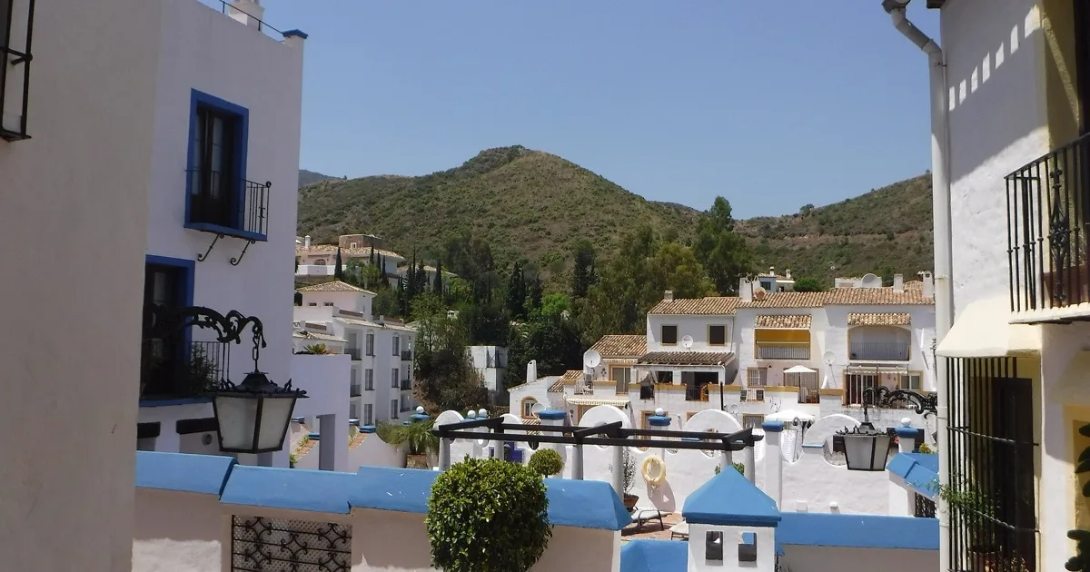 Whitewashed houses with blue trim and terracotta roofs in the hills of Benahavís above Marbella, with a green mountain backdrop — Benahavís villa escort bookings guide 2026