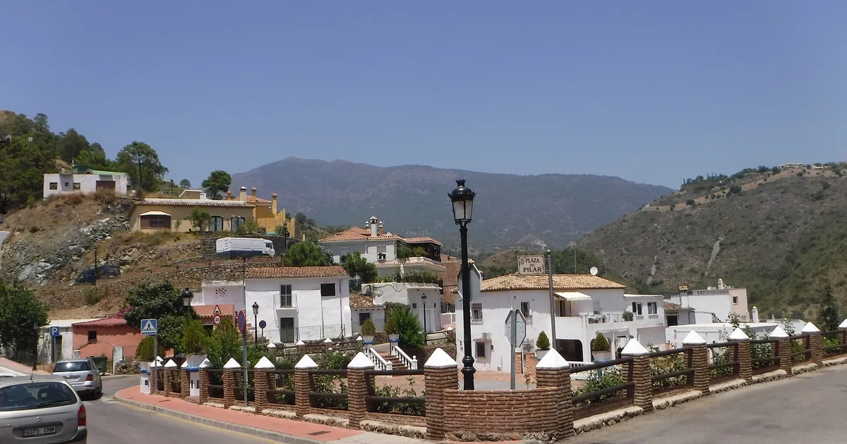 Whitewashed houses and street lamps on the road into Benahavís village, with green hills behind