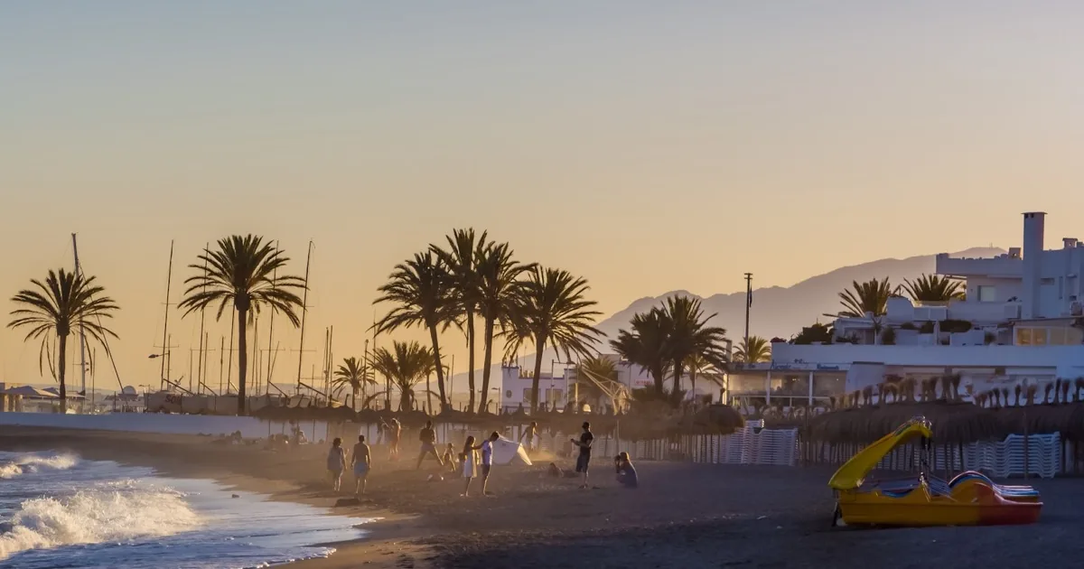 Marbella beachfront at sunset with palm trees and white five-star resort facades — Golden Mile escort outcall guide 2026