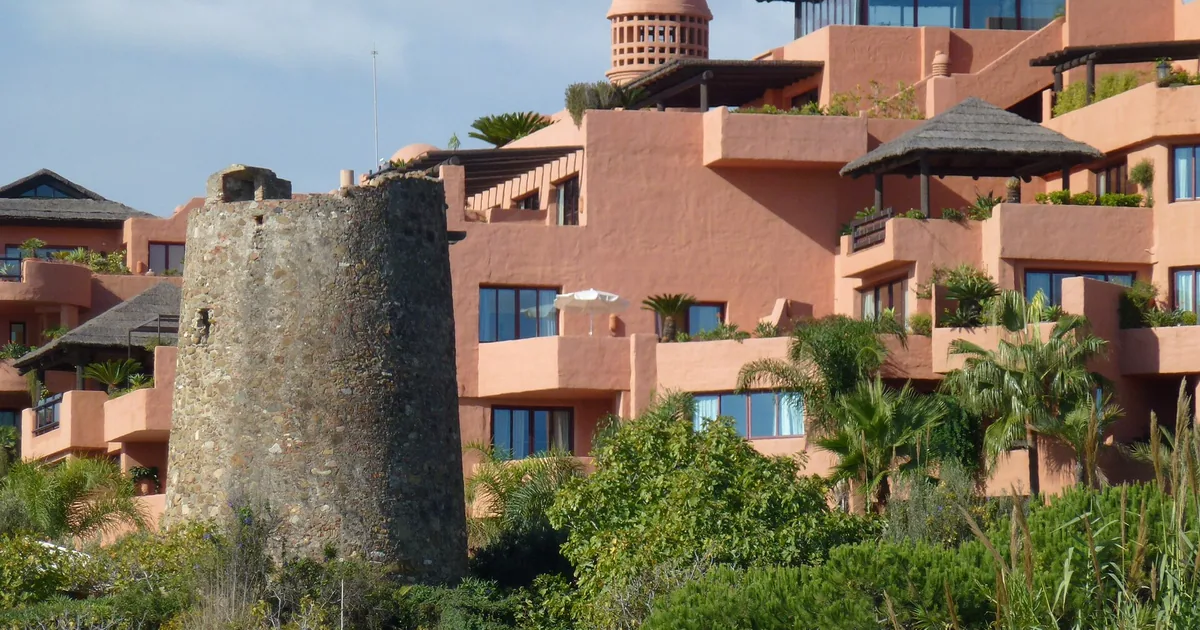 Terracotta terraces of the former Kempinski Hotel Bahía in Estepona, now Hacienda del Mar, beside an old stone watchtower among palms
