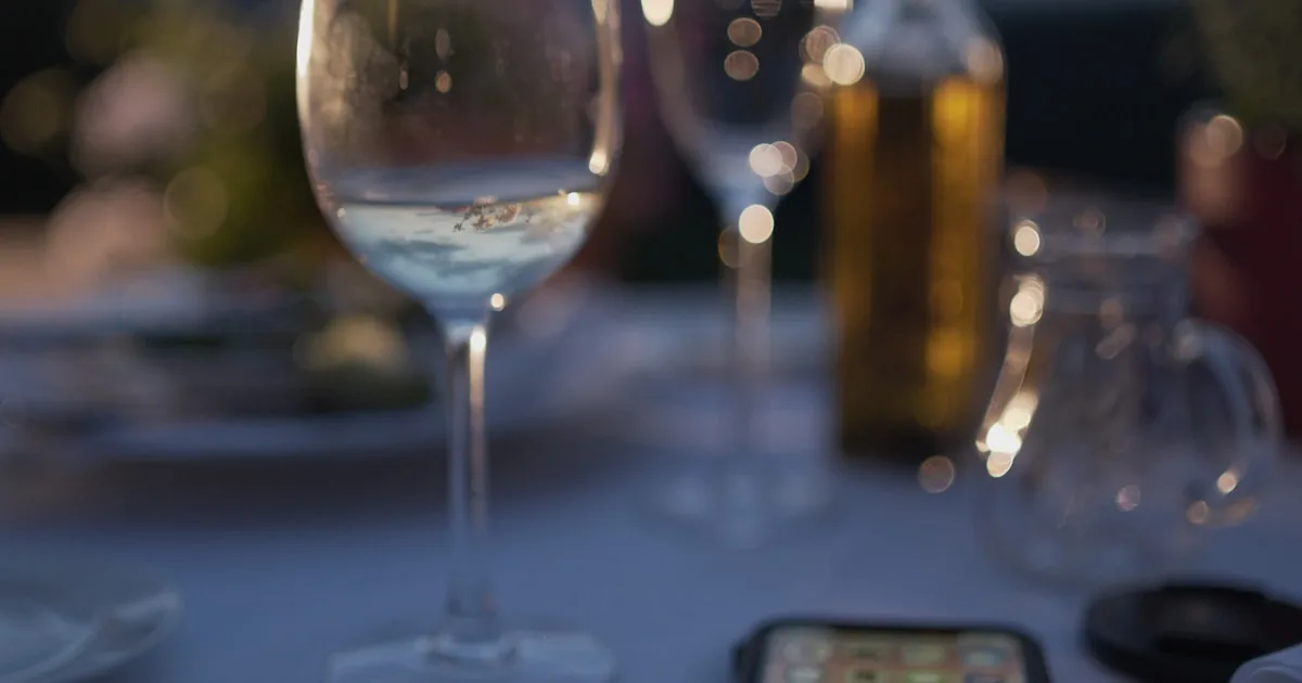 Smartphone beside wine glasses on a candlelit dinner table — Marbella escort WhatsApp booking templates for 2026