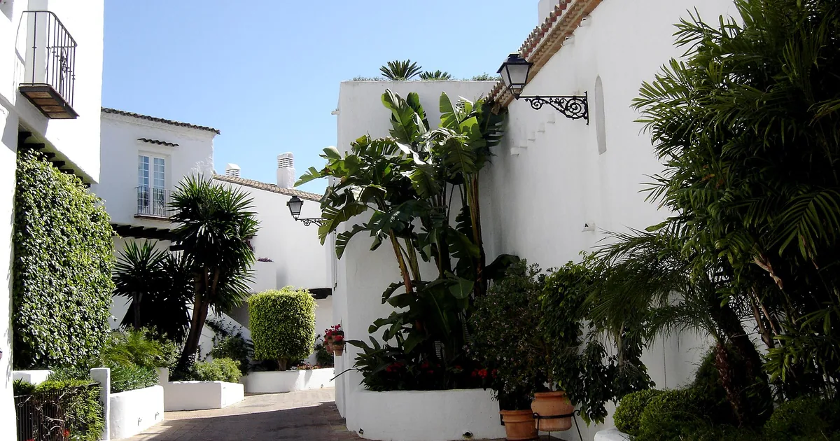 Whitewashed walkway with palms and flowerpots between the village-style buildings of Puente Romano Beach Resort, Marbella